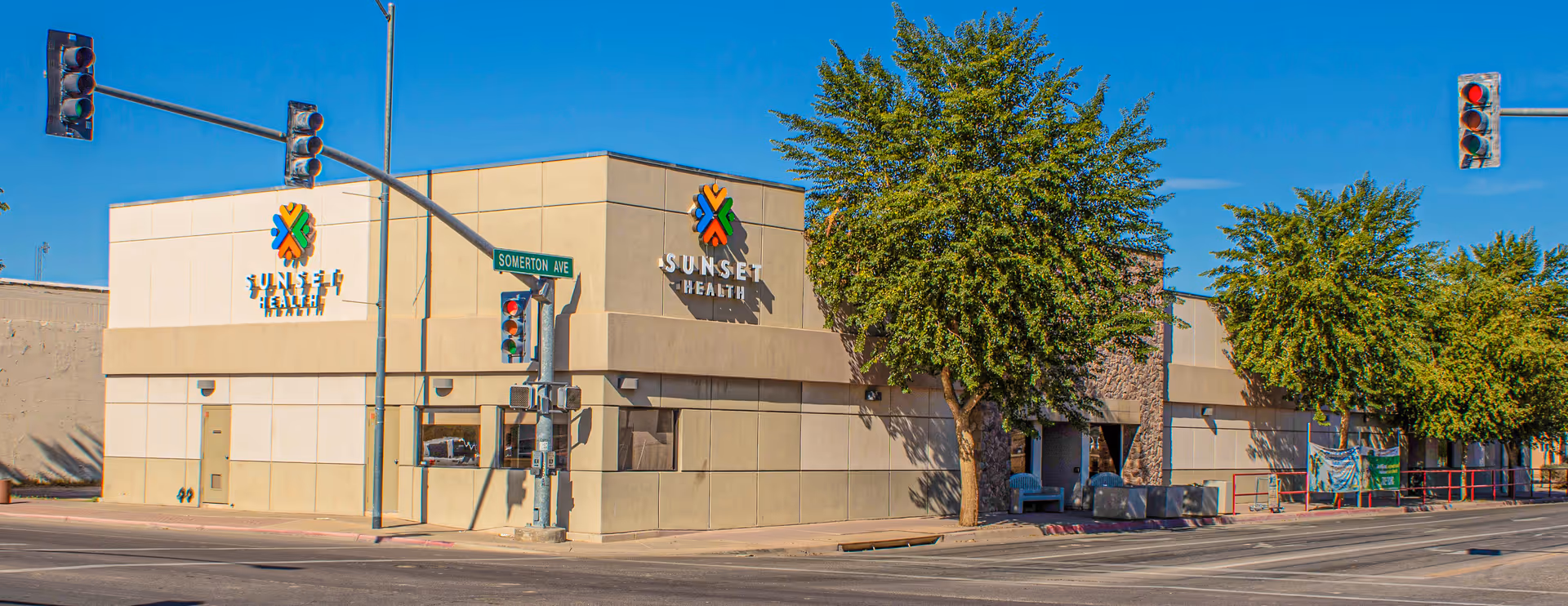 Exterior view of a Sunset Health facility on a tree-lined street corner.