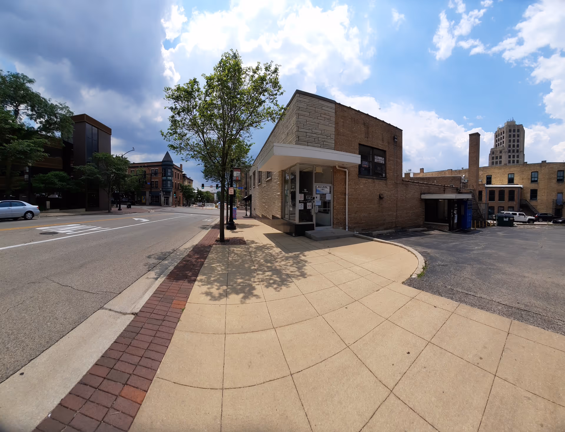 Brick storefront on a curved sidewalk with trees and a street.