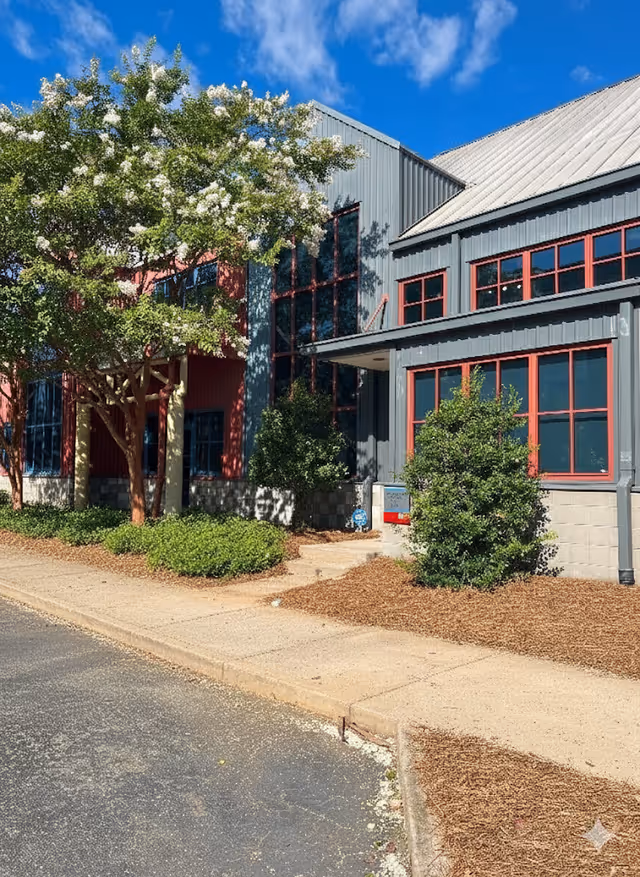 Exterior view of BrightStar Care facility front: grey siding, red-framed windows, trees, and sidewalk.