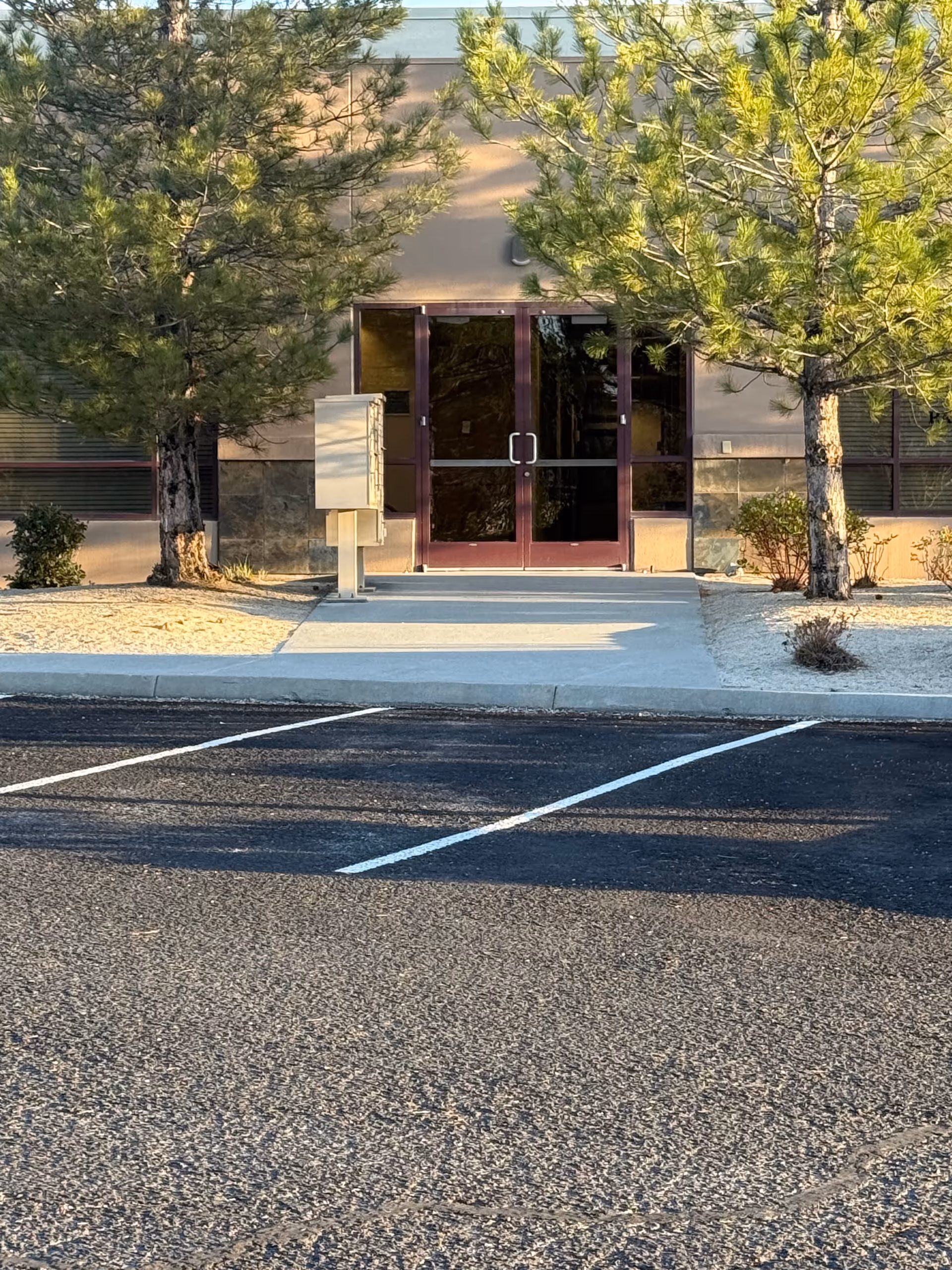 Parking lot leads to the facility entrance with glass doors and trees.