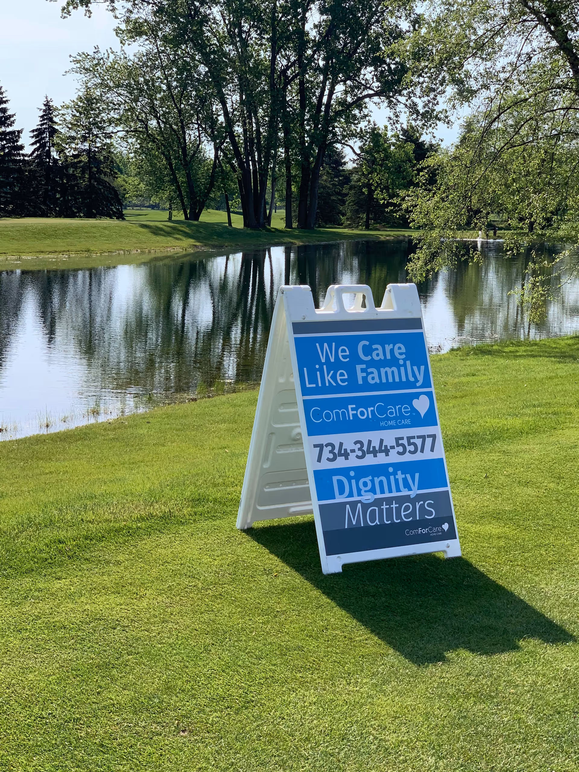 Outdoor view of a ComForCare sign on a grassy lawn beside a lake.