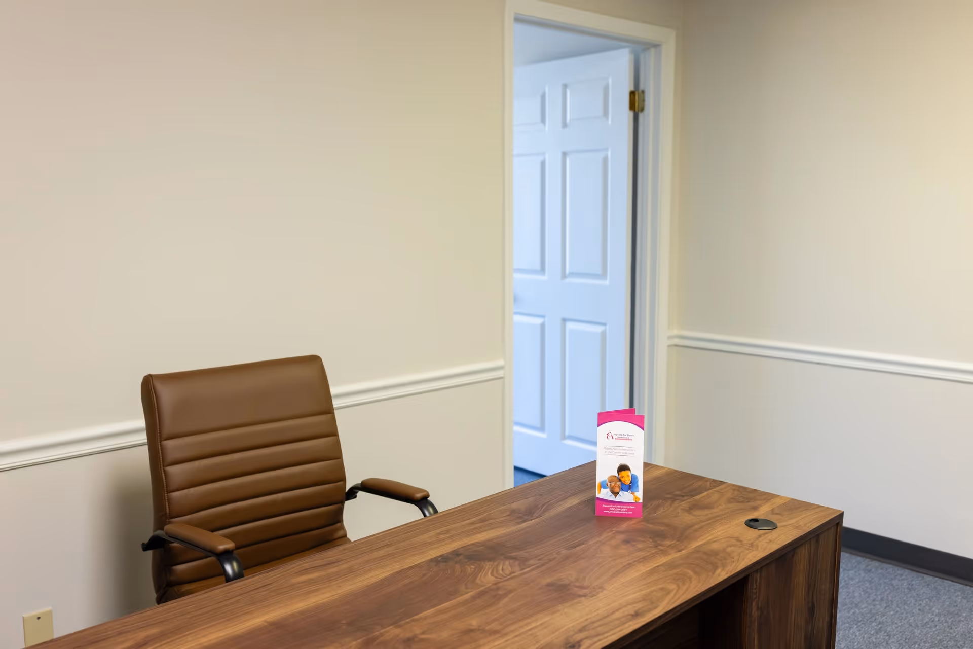 Wooden desk and brown chair in a quiet interior office with a brochure on the desk.