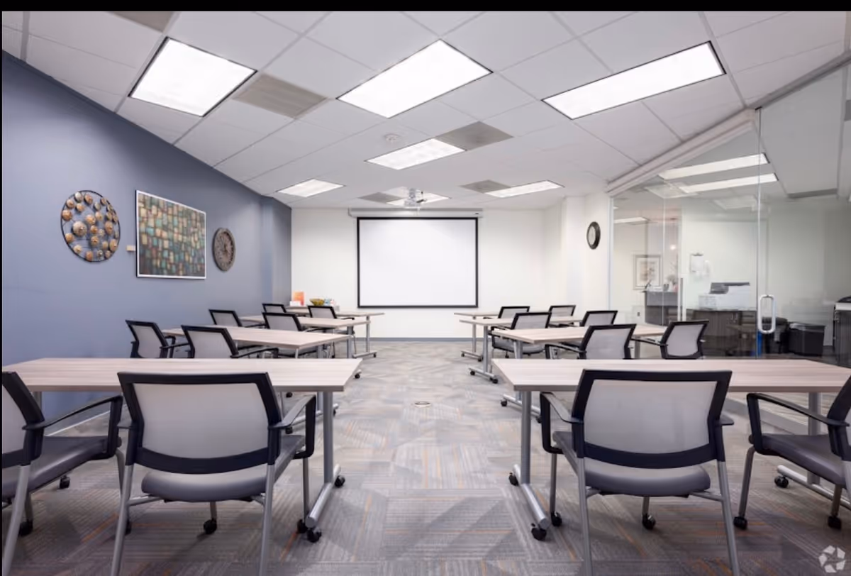 A modern training room with desks, chairs, and a projection screen at the front.