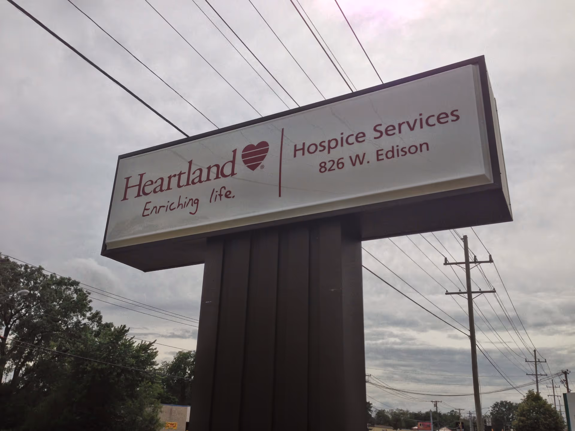 Outdoor Heartland Hospice Services sign on a tall pillar with power lines in the background.