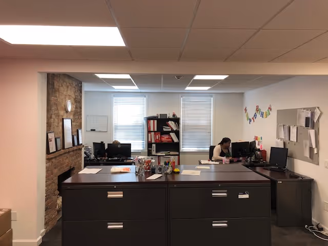 An indoor office reception area with desks, computers, filing cabinets, and a brick fireplace.