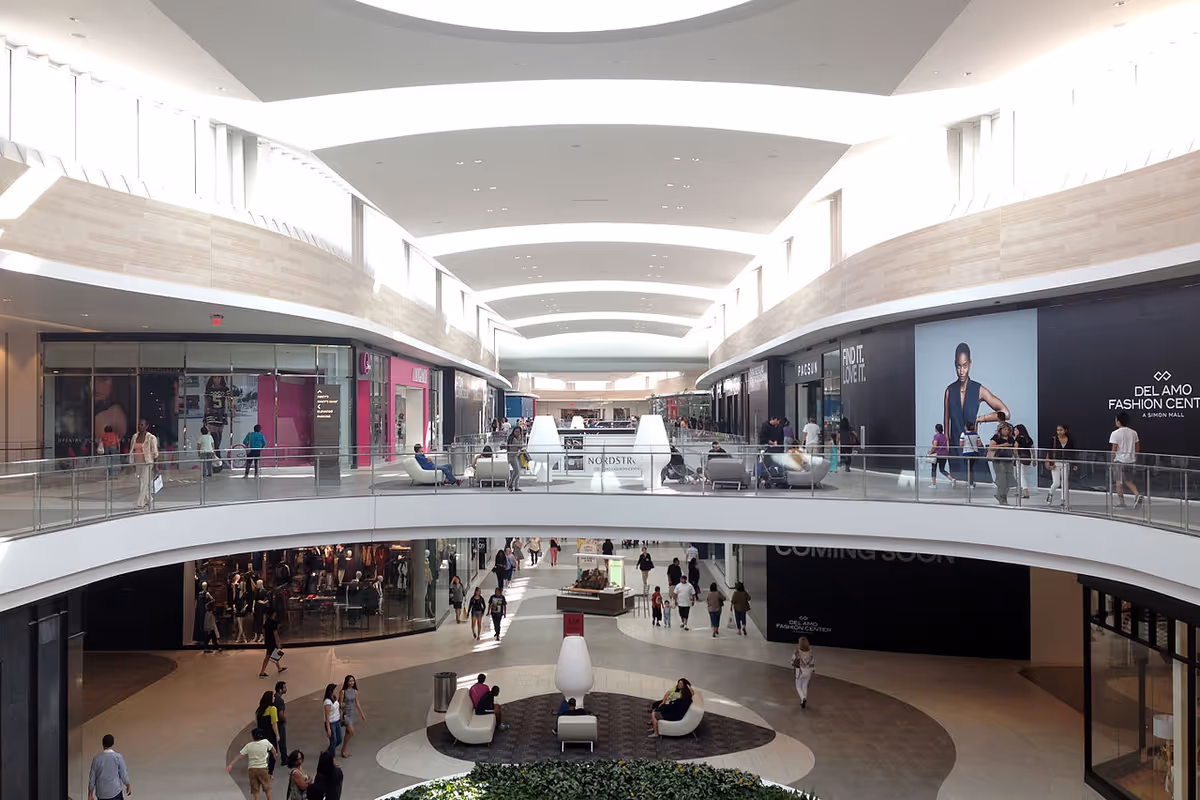 Bright multi-level shopping mall interior with storefronts, balconies, and shoppers.