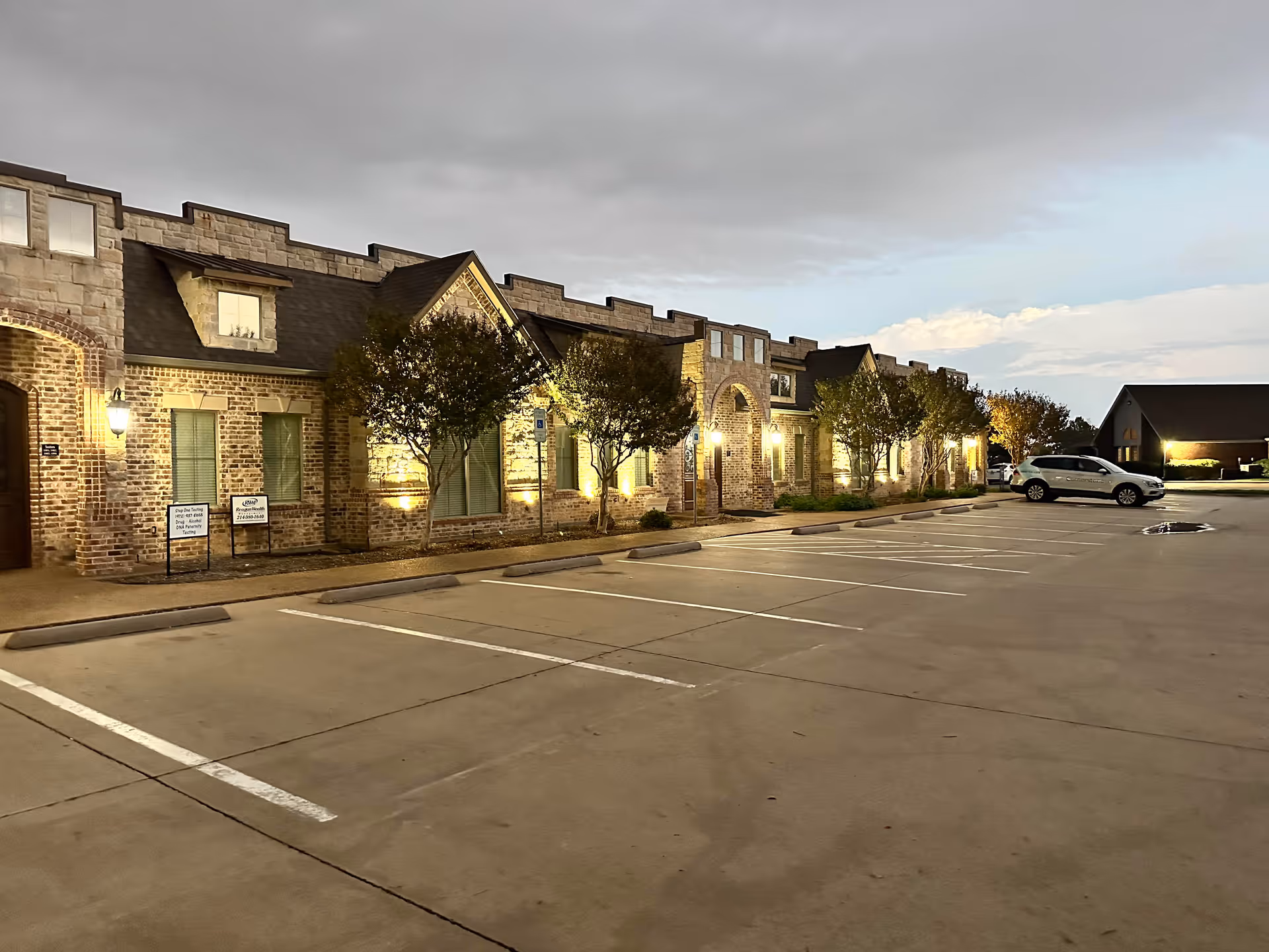 Brick senior living building extends across the parking lot under a cloudy sky.
