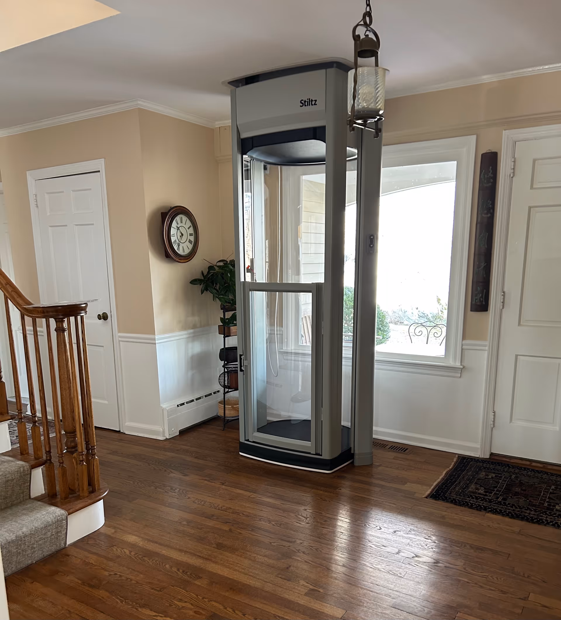 Residential foyer with a vertical home elevator, wooden stairs, beige walls, and hardwood floor.