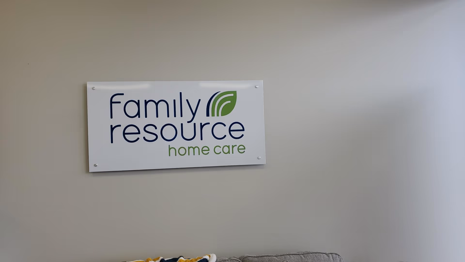 Interior wall with a Family Resource Home Care sign and partial couch seating.