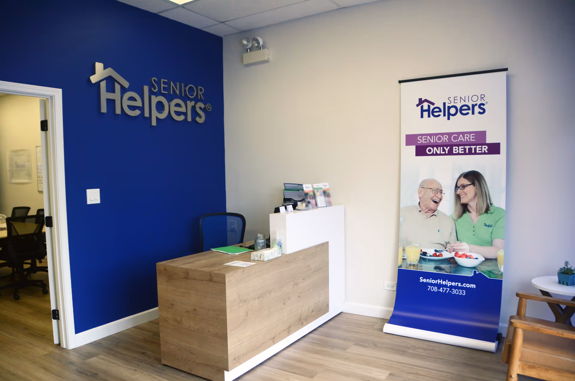 Reception area with blue wall, Senior Helpers logo, and promotional banner inside facility.