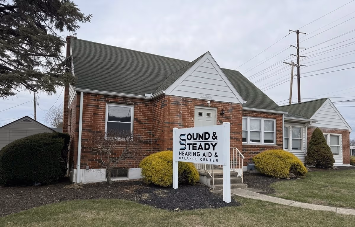 Brick senior living facility front with a sign reading Sound & Steady Hearing Aid.