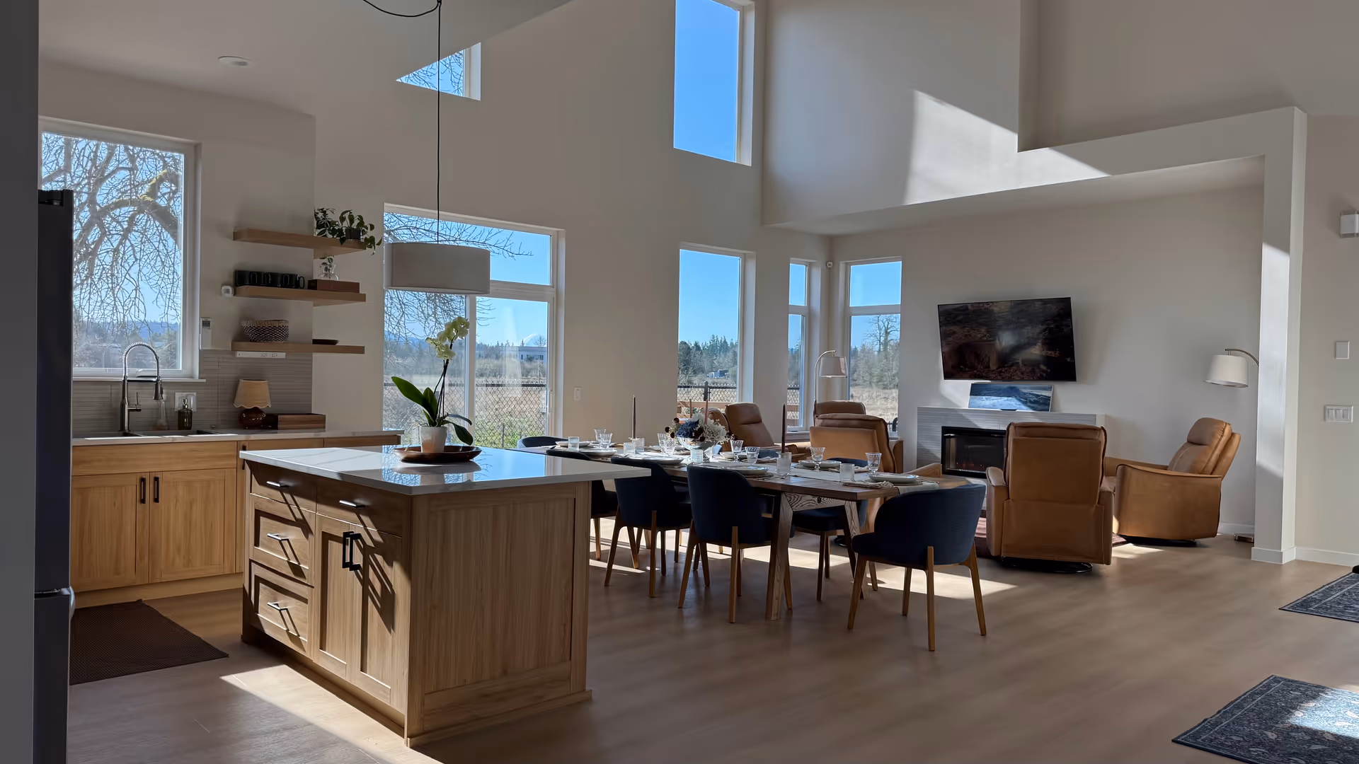 Open, sunlit senior living common area with kitchen island, dining table, and lounge seating.
