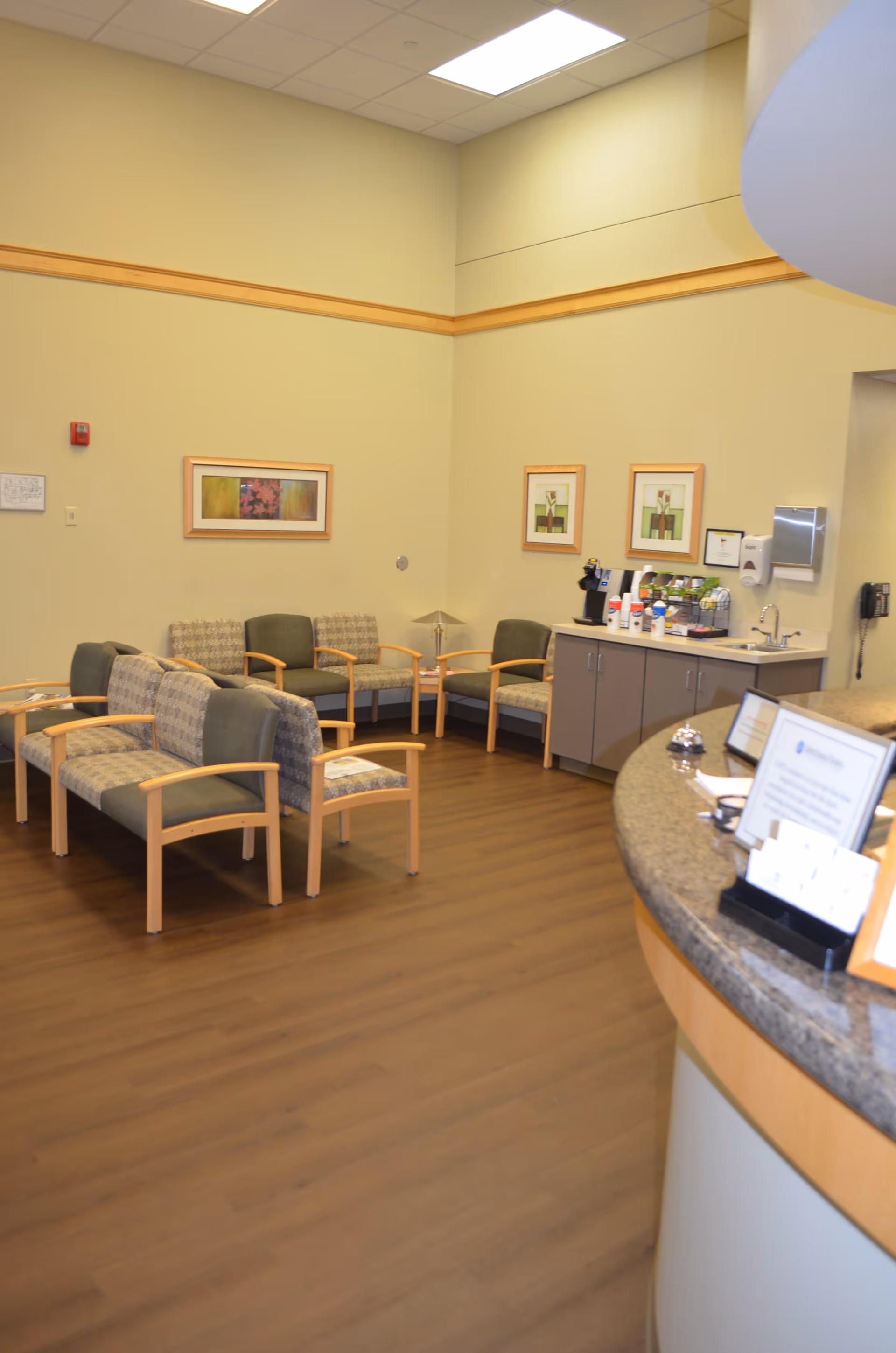 Lobby waiting area with beige walls, green chairs, and a curved reception counter.