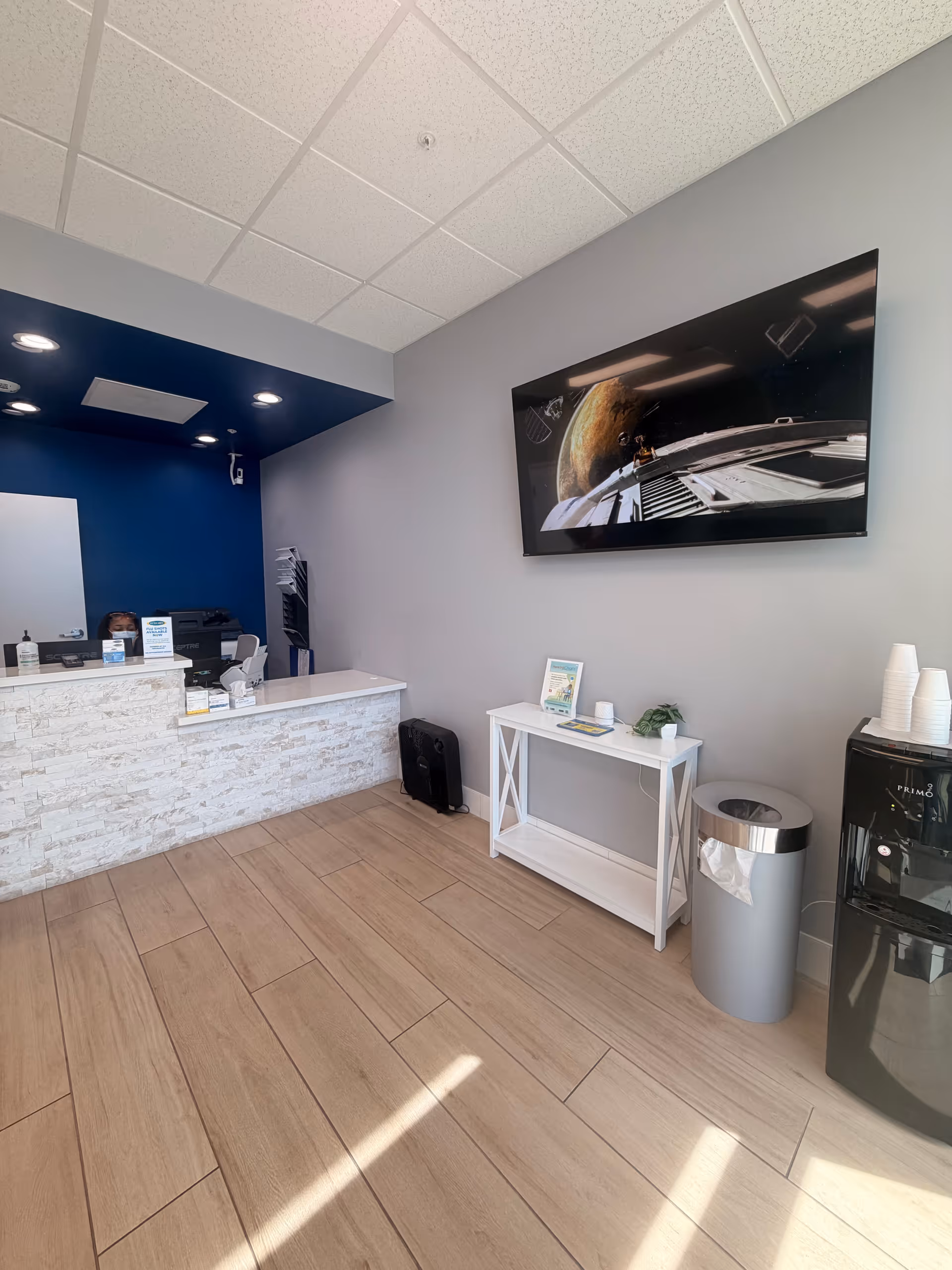 Reception area with a white front desk, wall TV, console table, and a staff member.