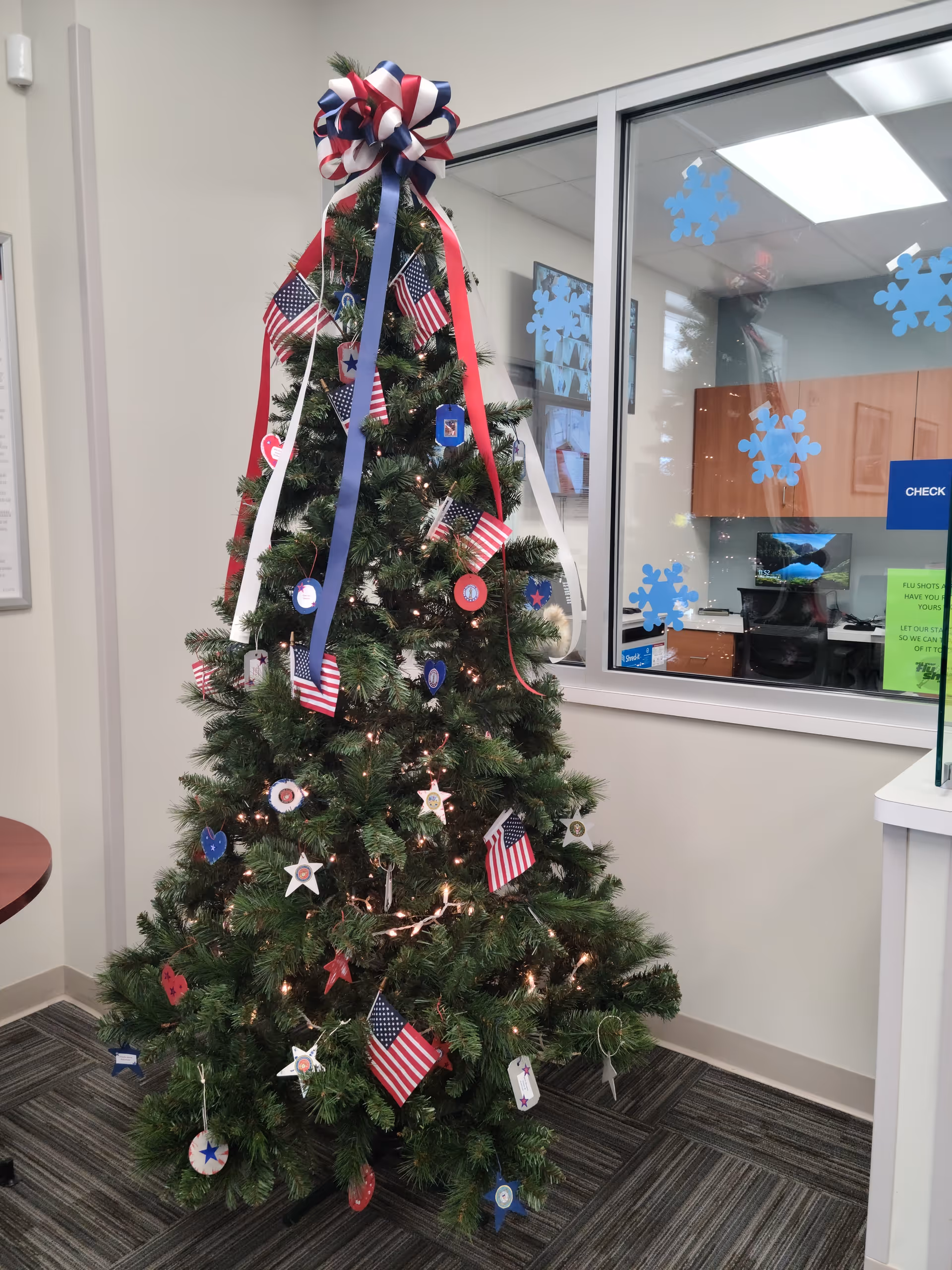 Decorated Christmas tree with ribbons, ornaments, and American flags in a hospice facility lobby.