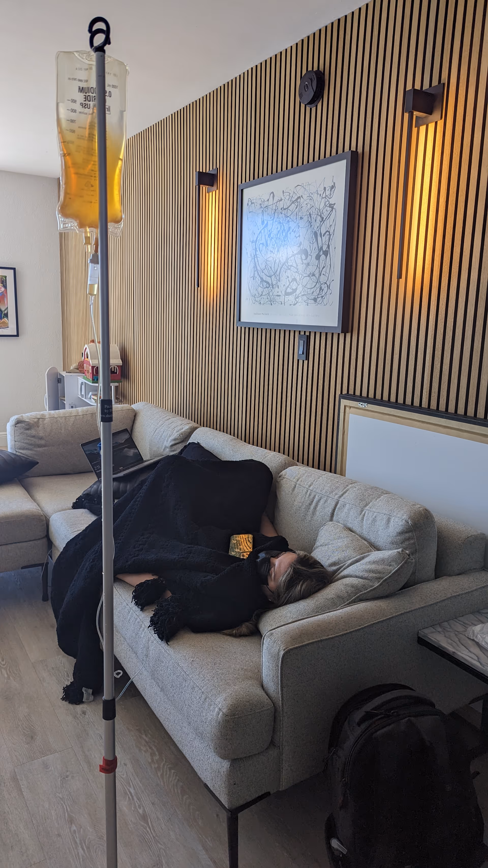Senior resident sleeping on a beige sofa beside an IV stand in a modern living room.
