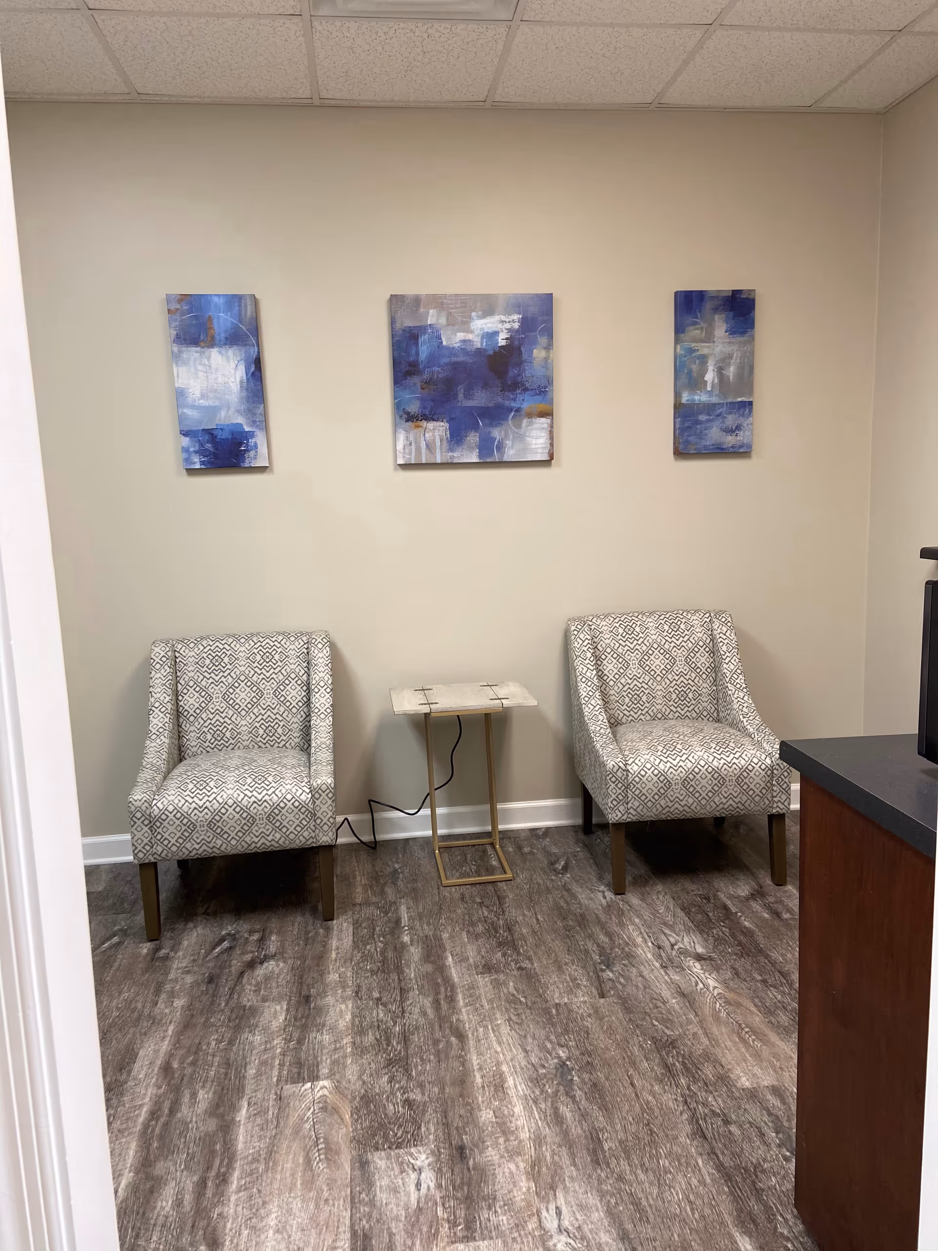 Two patterned armchairs flank a small marble-topped table in a beige-walled waiting area.