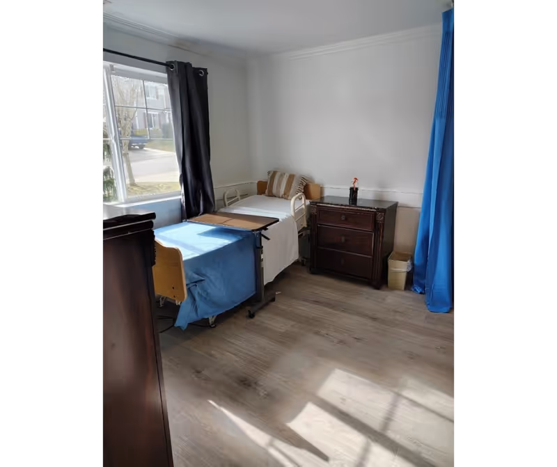 A bright bedroom with an adjustable hospital bed, blue curtains, and a dark dresser.