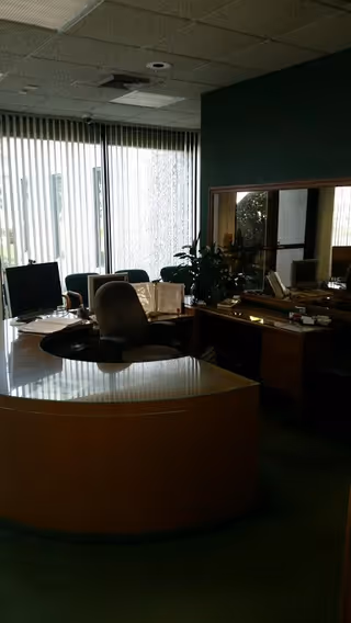 Curved reception desk with computers and vertical blinds in a dim office.