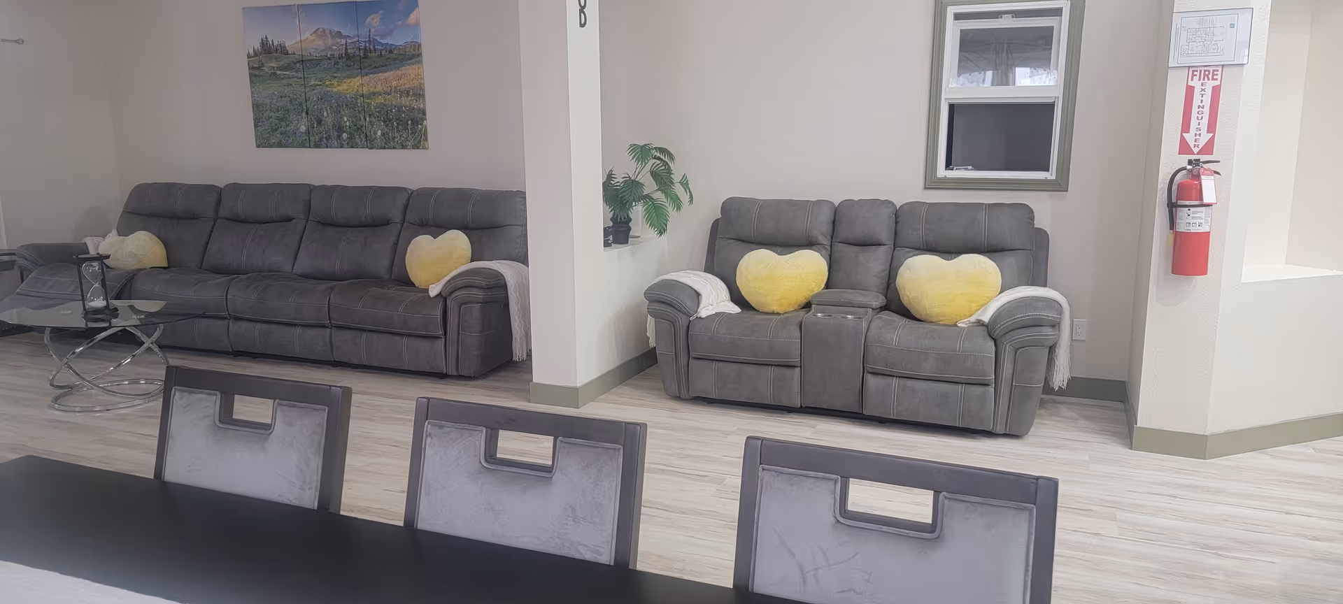 Bright living room with two gray sofas, yellow heart pillows, and a dining table.