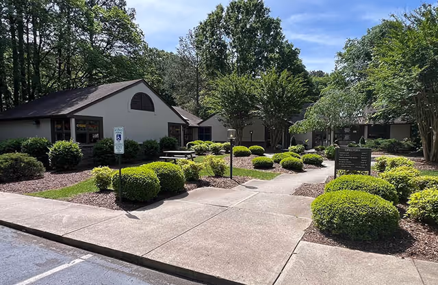 Exterior view of a senior living facility with manicured shrubs and a paved walkway.