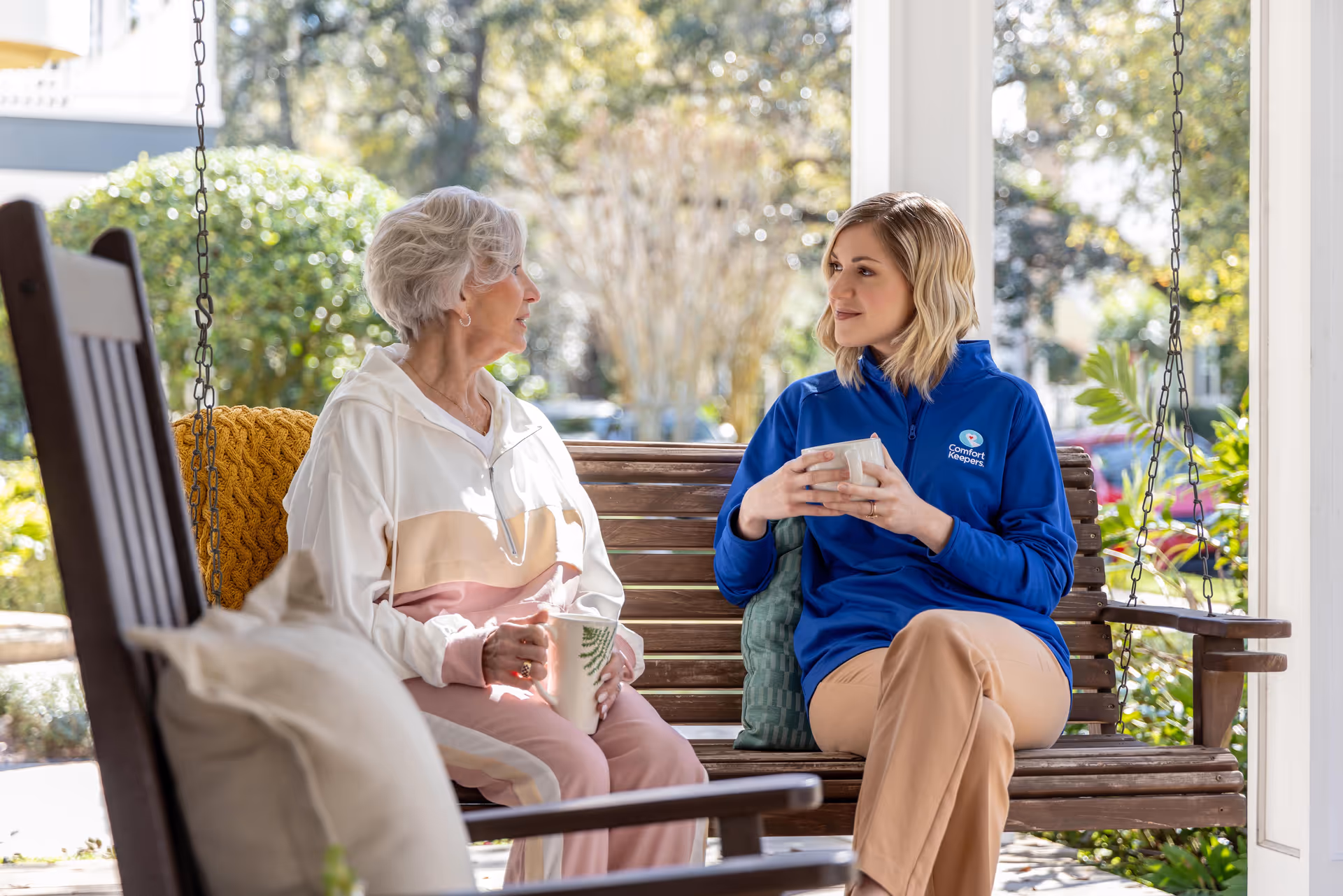 Caregiver and resident chat on a porch swing outdoors.