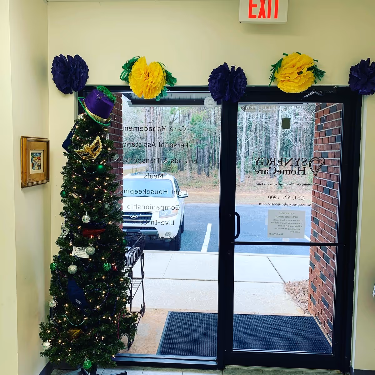 Decorated interior entry with a Christmas tree beside glass doors and colorful paper pompoms.