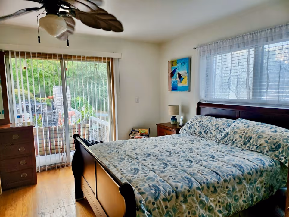 Bright bedroom with a large bed, nightstand, ceiling fan, and sliding glass door to patio