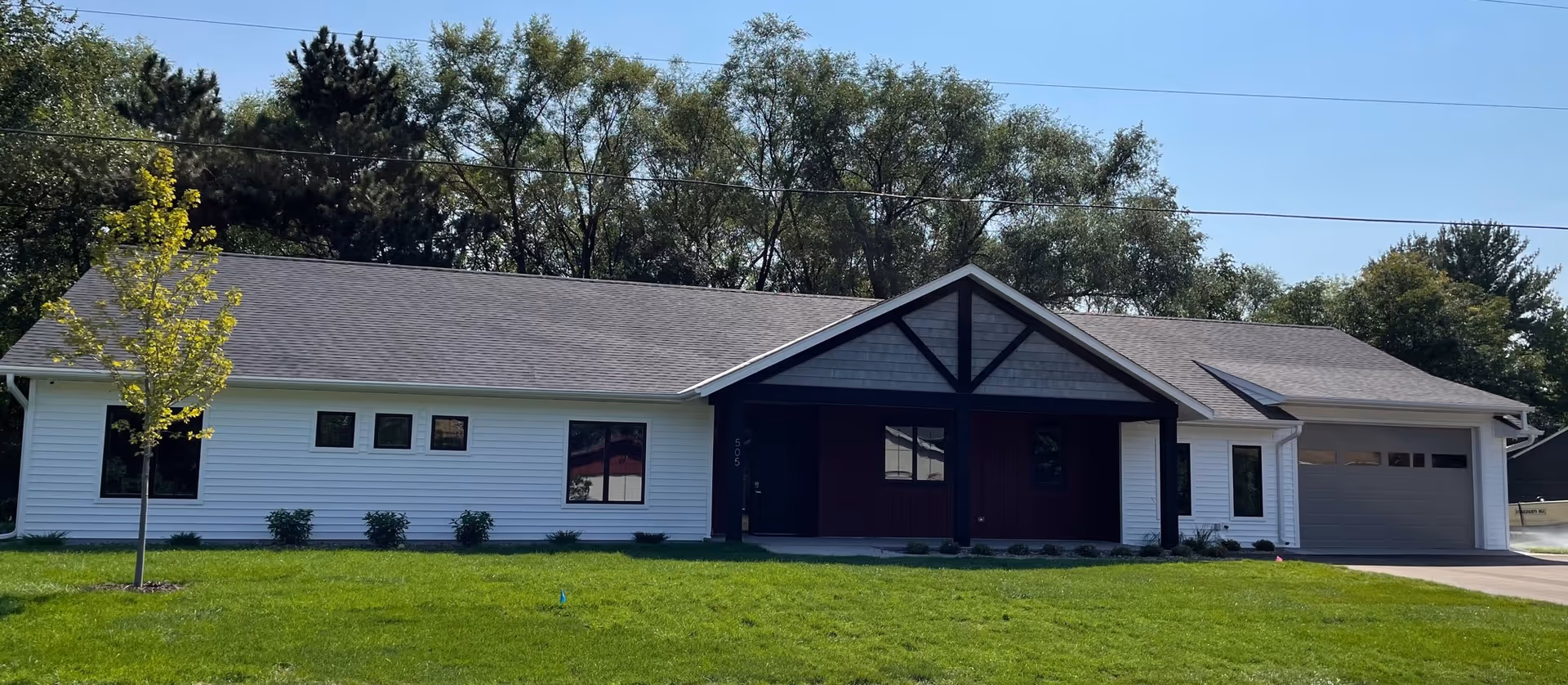 Single story senior living facility with a dark trim entrance, light siding, and a front lawn.