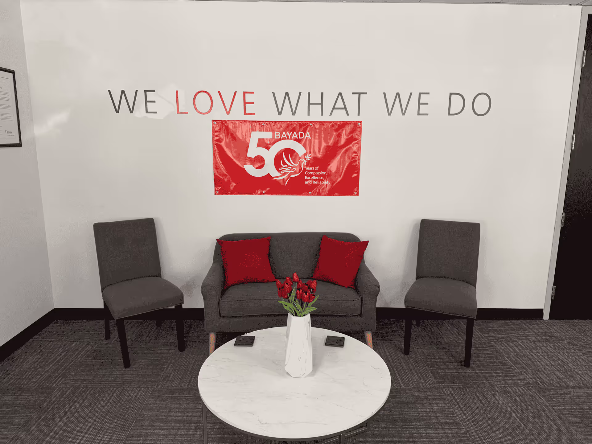 Lobby seating area with three chairs, a round marble table, tulips, and a red BAYADA banner.