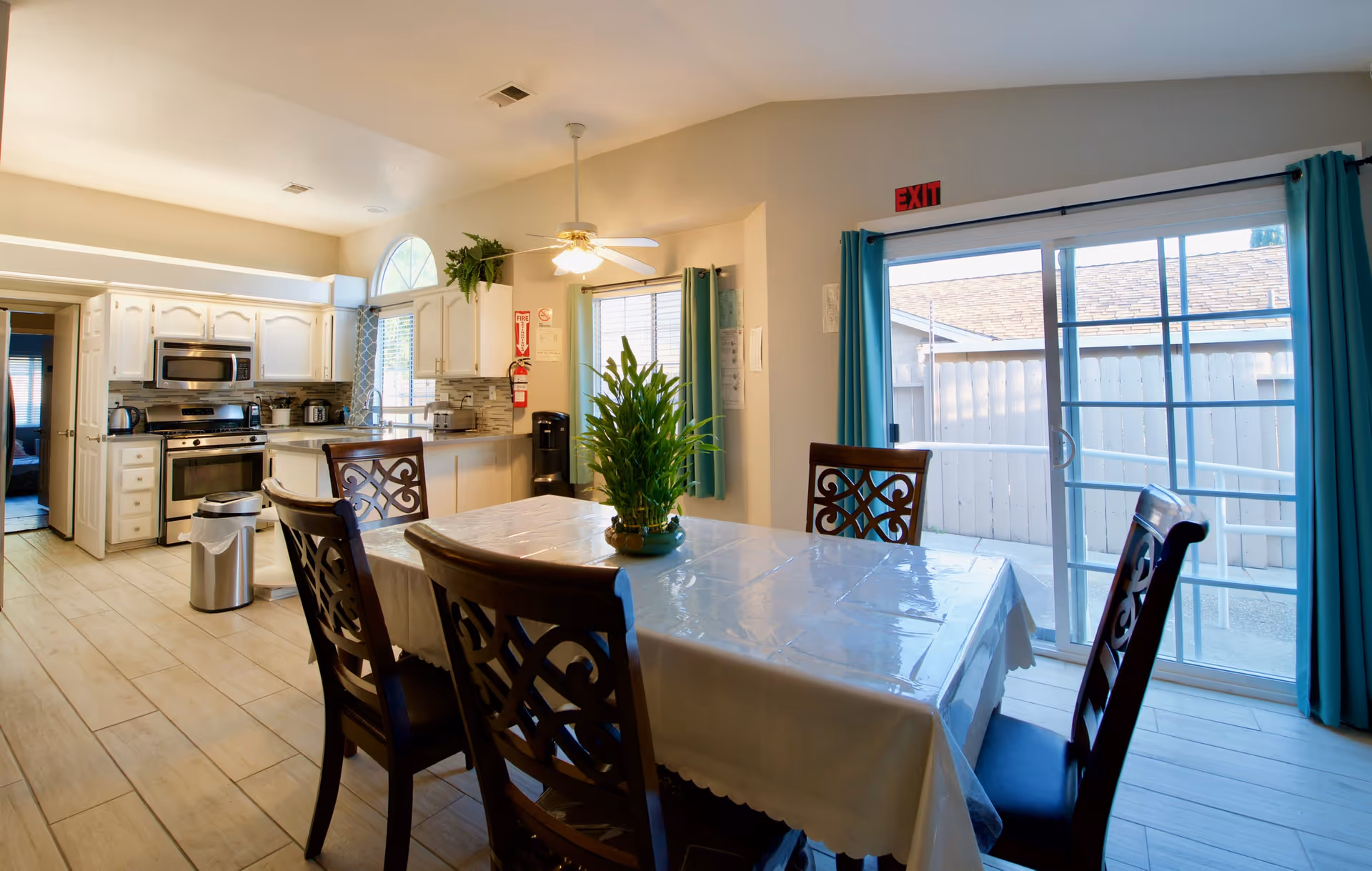 Bright dining area and kitchen in a senior living facility, with a table and sliding door.