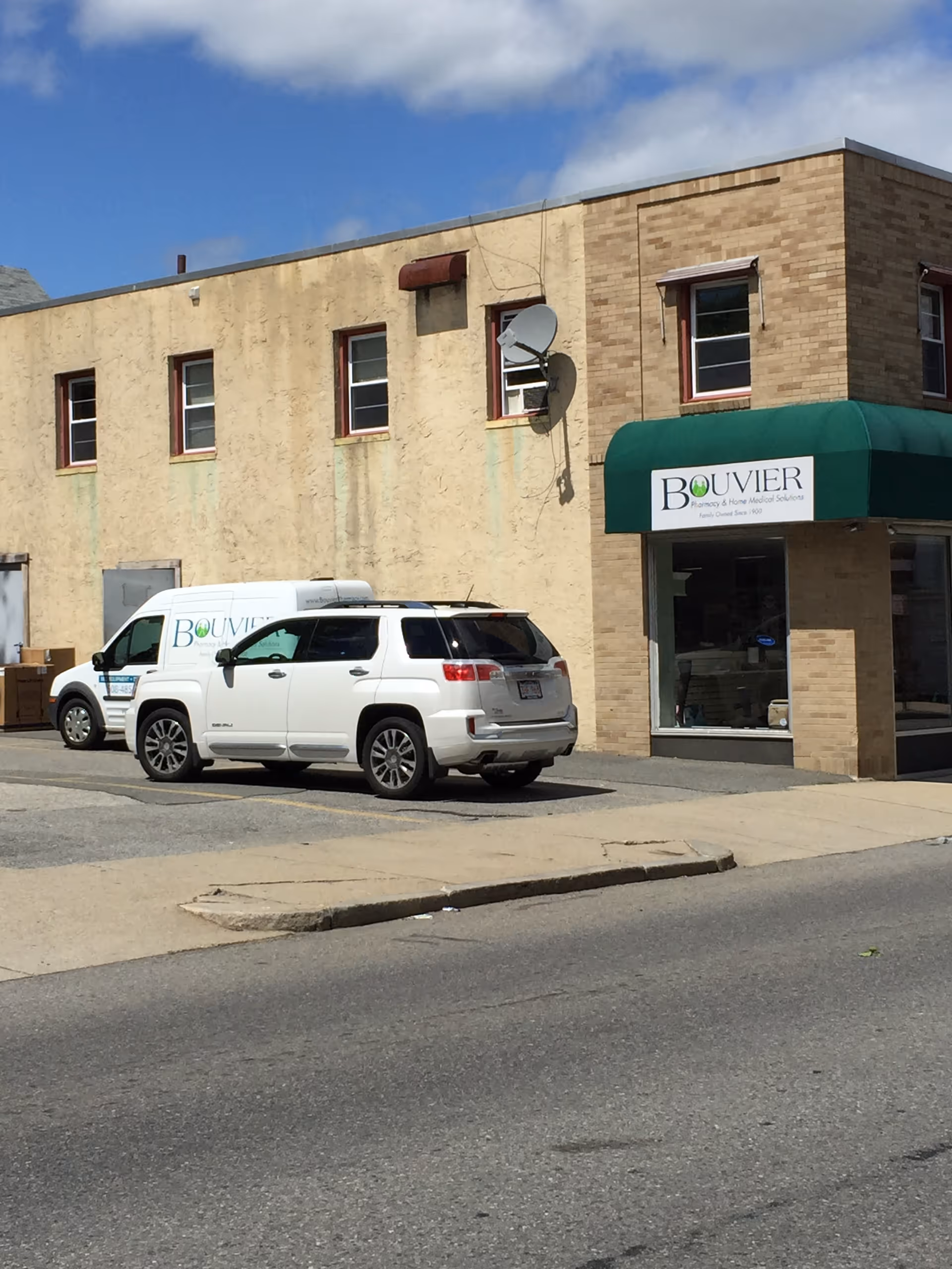 Exterior view of a building with a green awning and branded Bouvier Pharmacy vans.