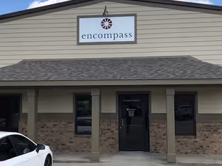 Front exterior of a beige building with an 'encompass' sign and entrance, a car parked nearby.
