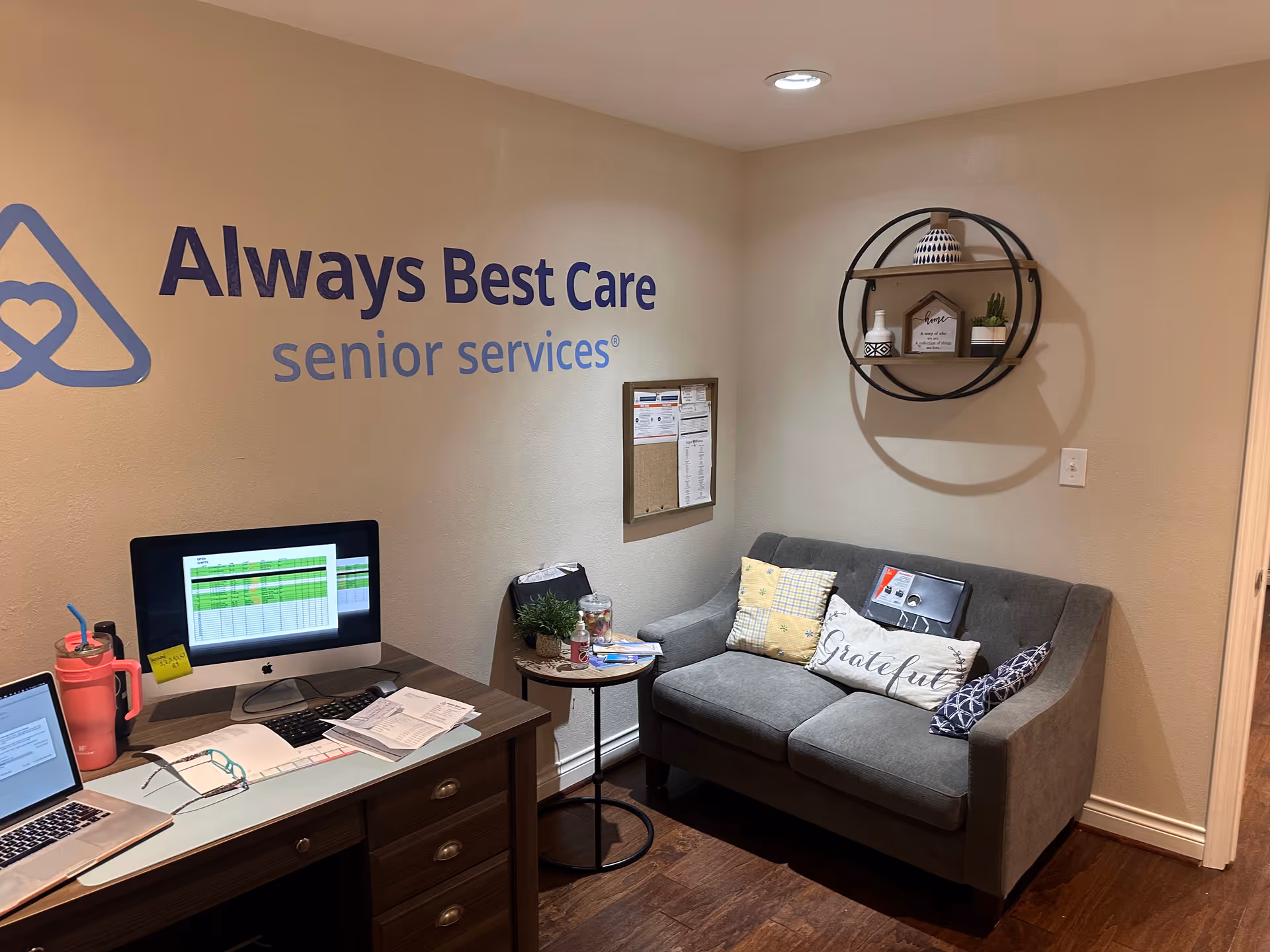 Office reception area with desk, computer, sofa, and Always Best Care logo on wall.