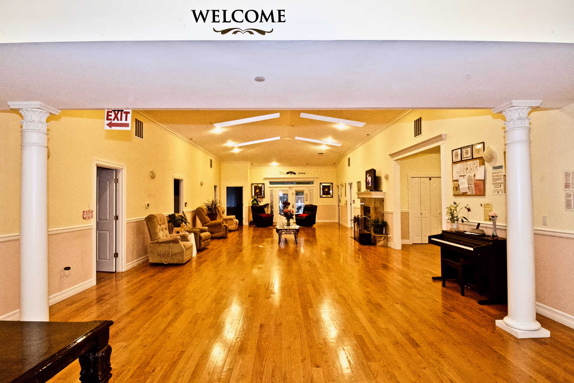 Well-lit senior living lobby with wooden floor, columns, and seating along the hallway.