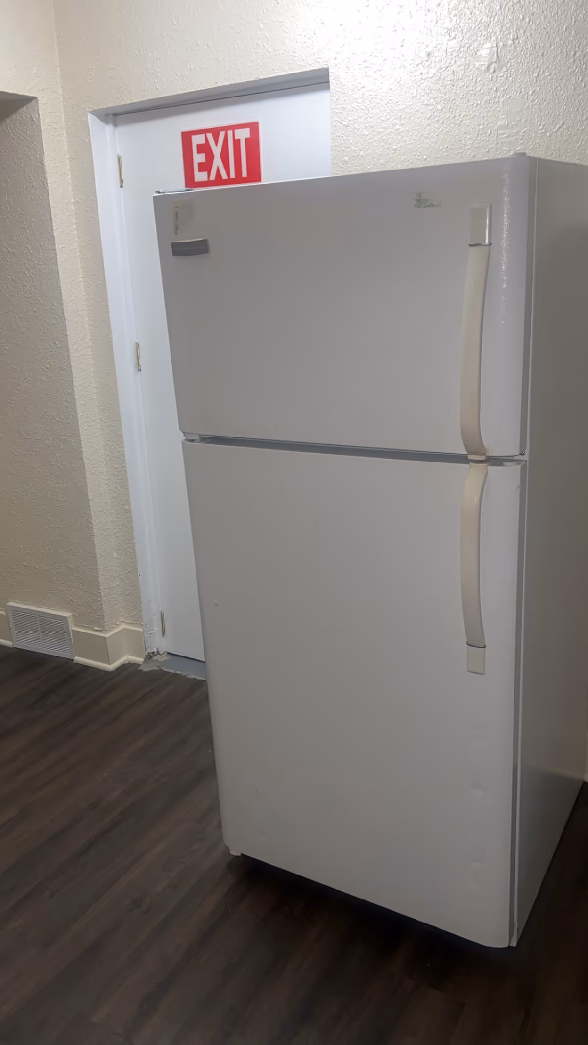 White refrigerator in a hallway beside an exit door and red EXIT sign.
