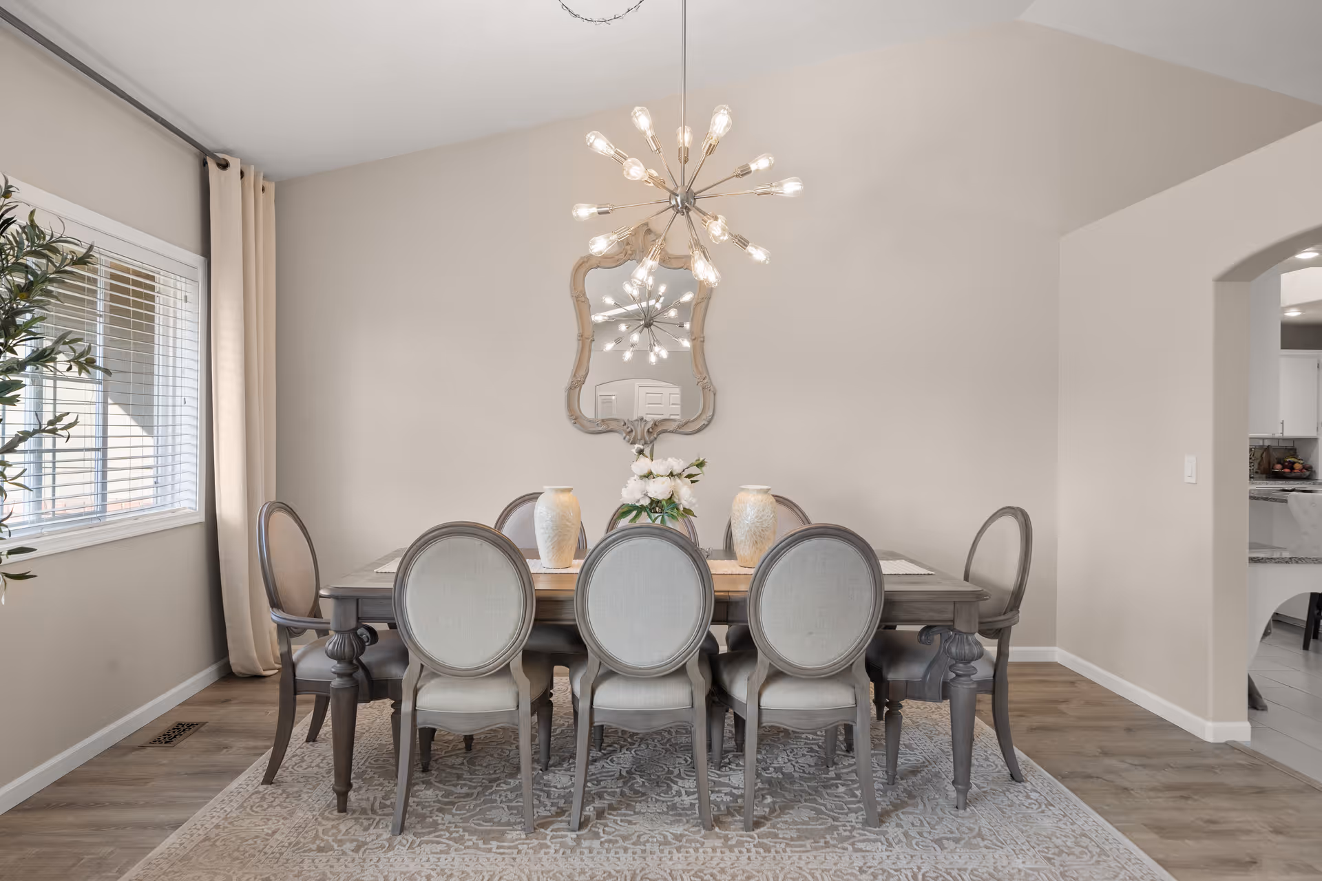 A stylish dining room with a long table, eight chairs, chandelier, and decorative mirror.
