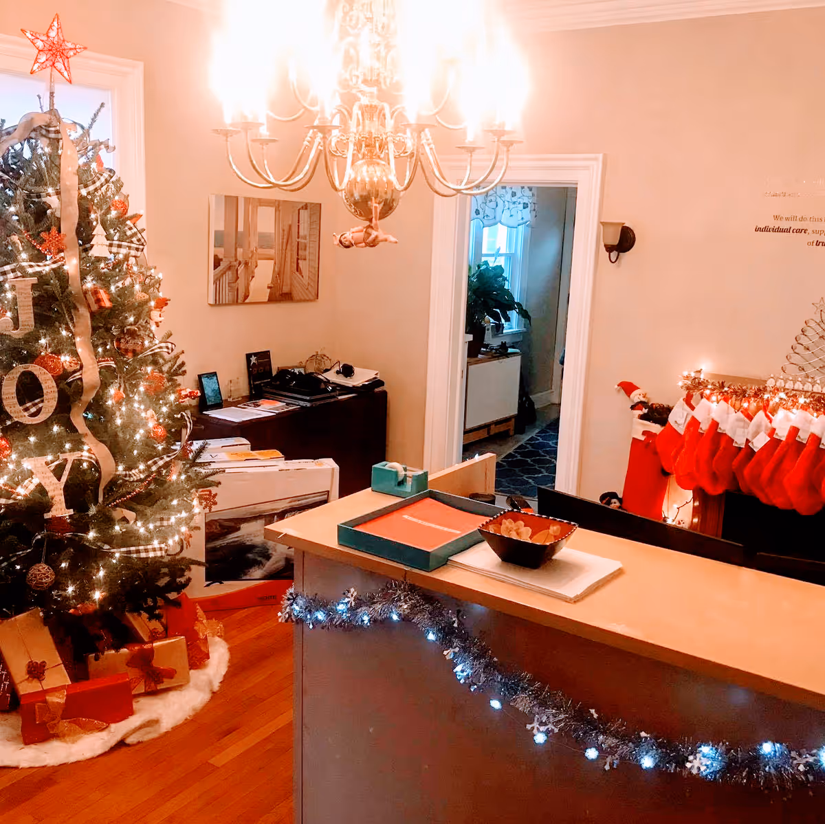 Christmas tree and festive decorations fill a cozy living room with a counter and chandelier.