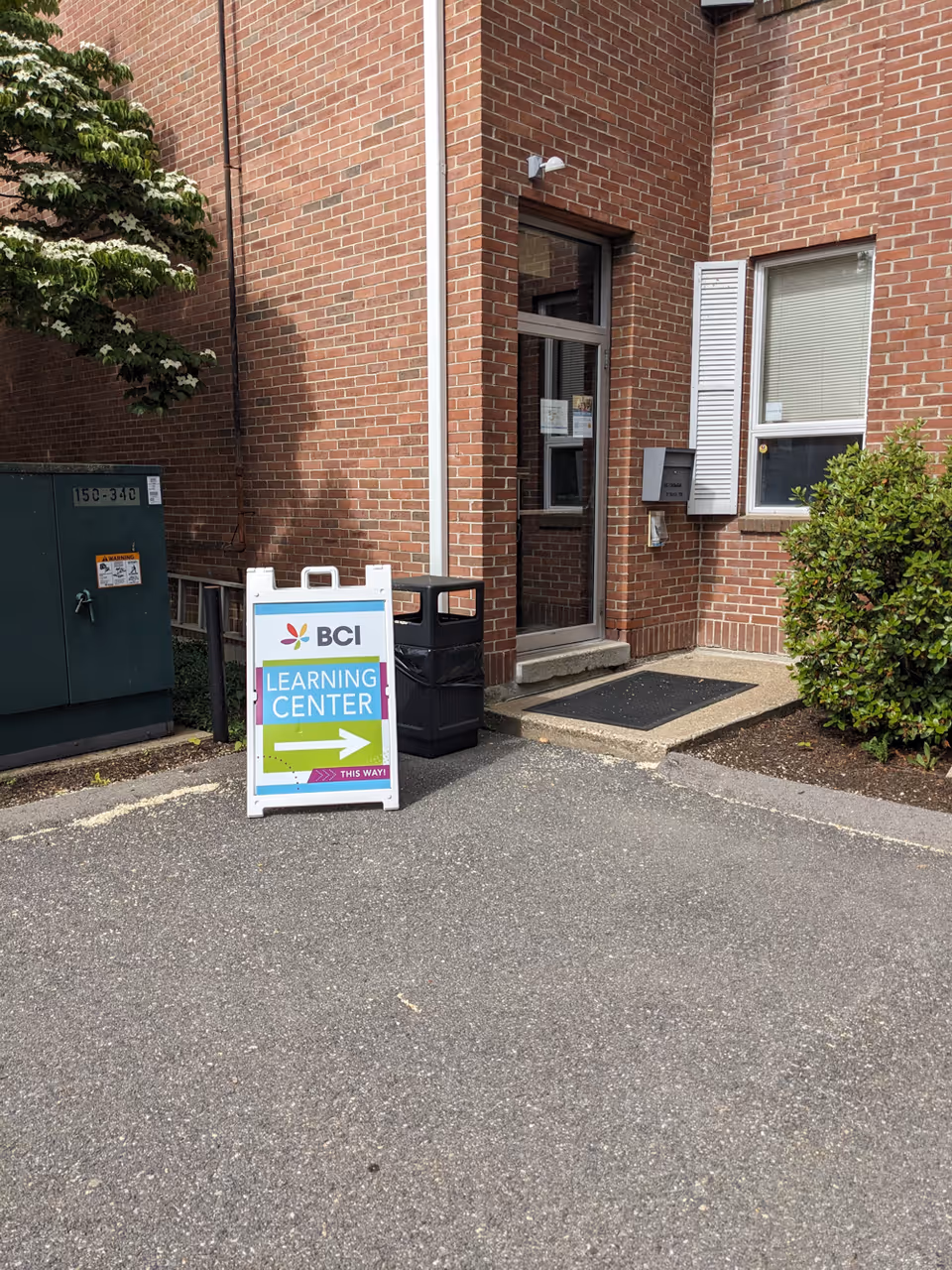 Brick building entrance with a standing sign for BCI Learning Center outside.
