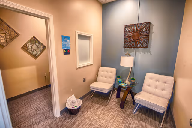 A small waiting area with two white lounge chairs, a glass table, and a lamp.