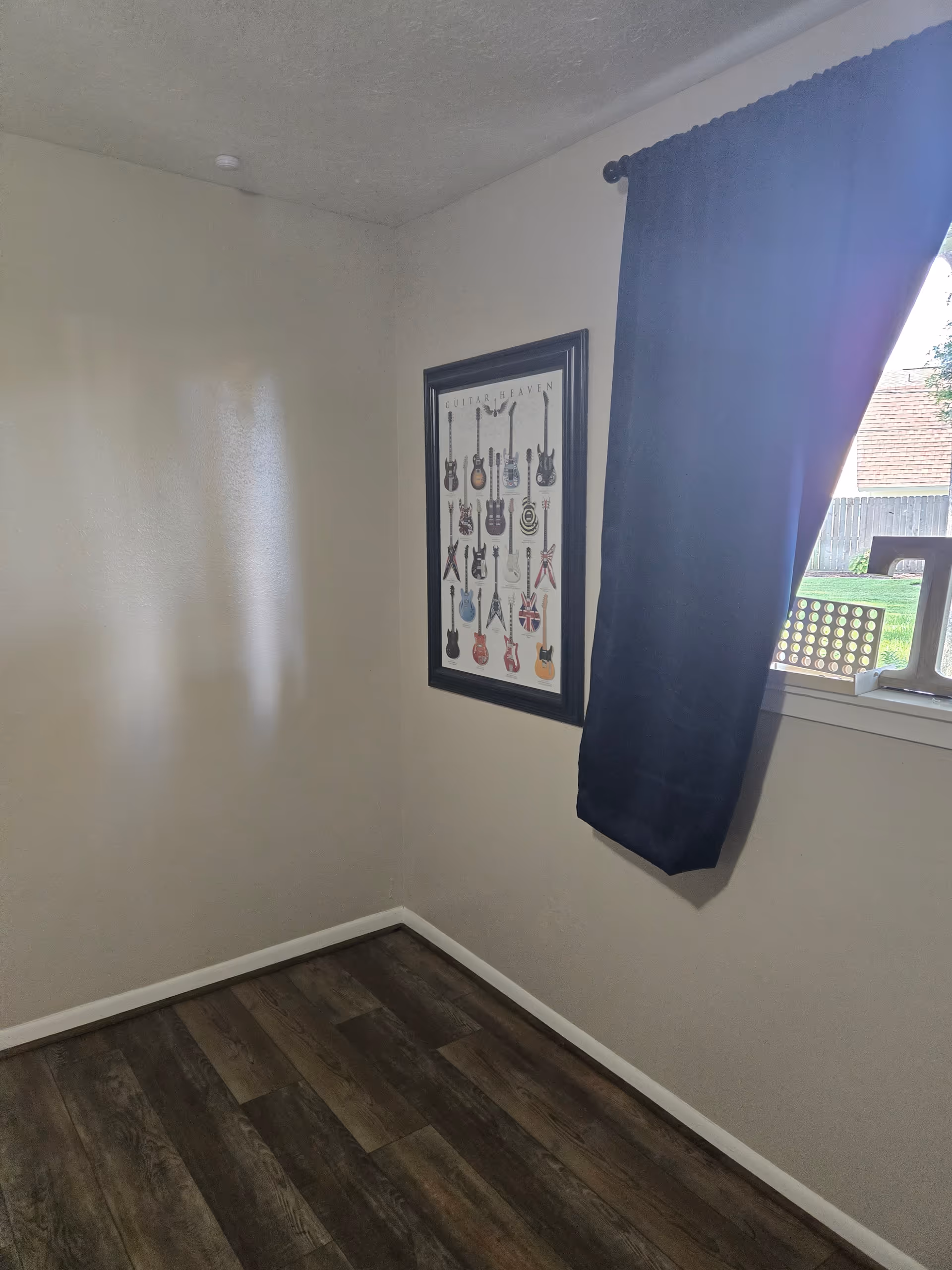 A small empty corner of a room with a guitar themed poster and window.