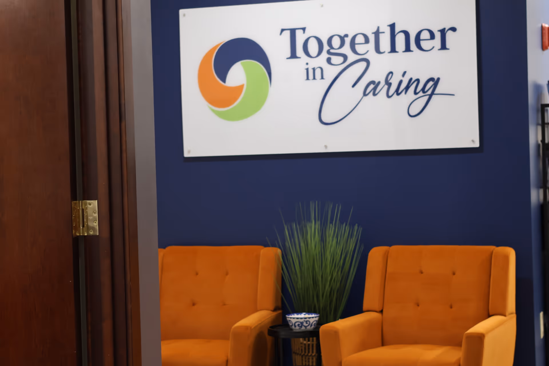 Blue wall interior with a Together in Caring sign and two orange armchairs.