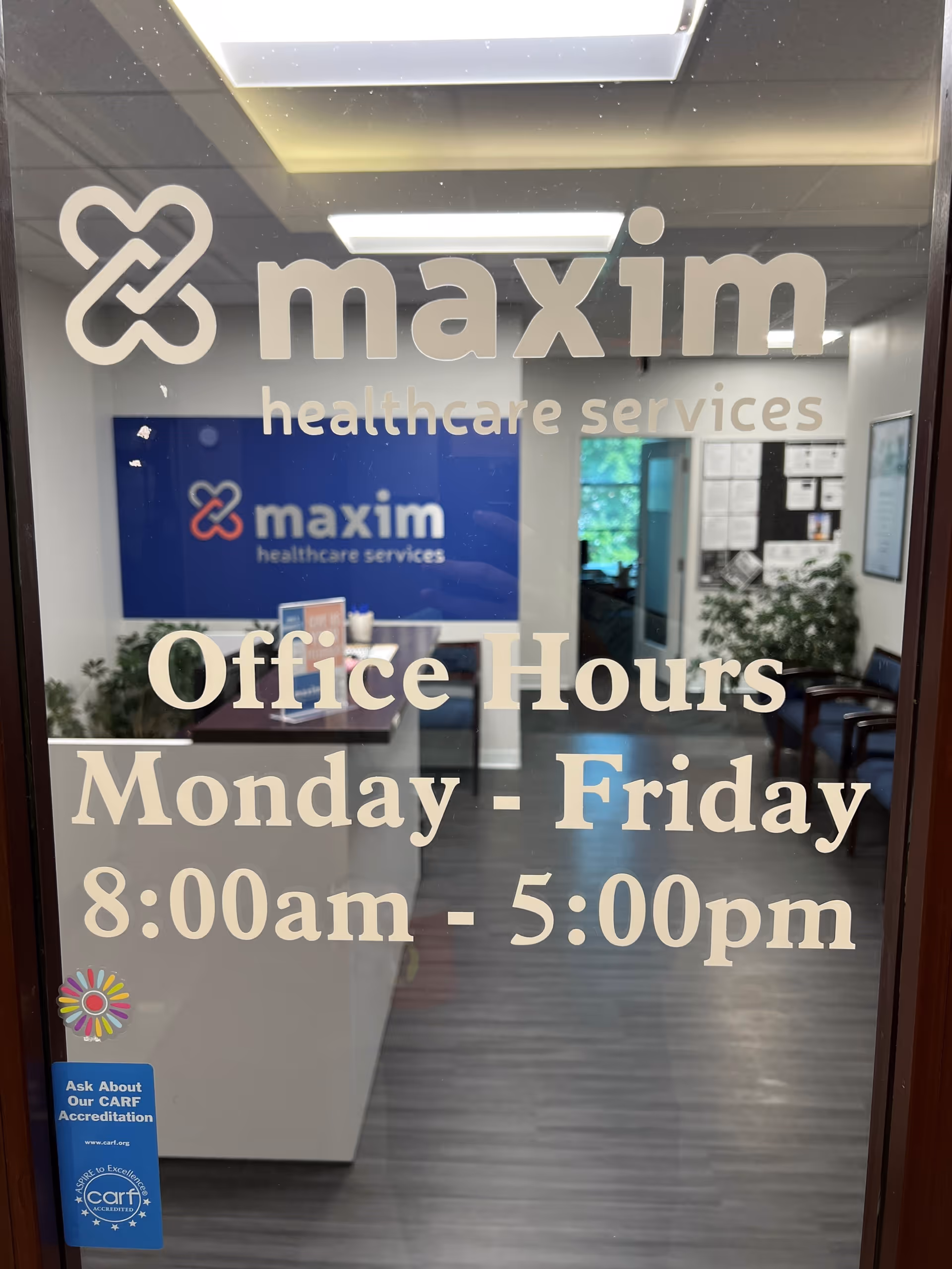 Interior lobby of Maxim Healthcare Services with office hours sign on glass door.