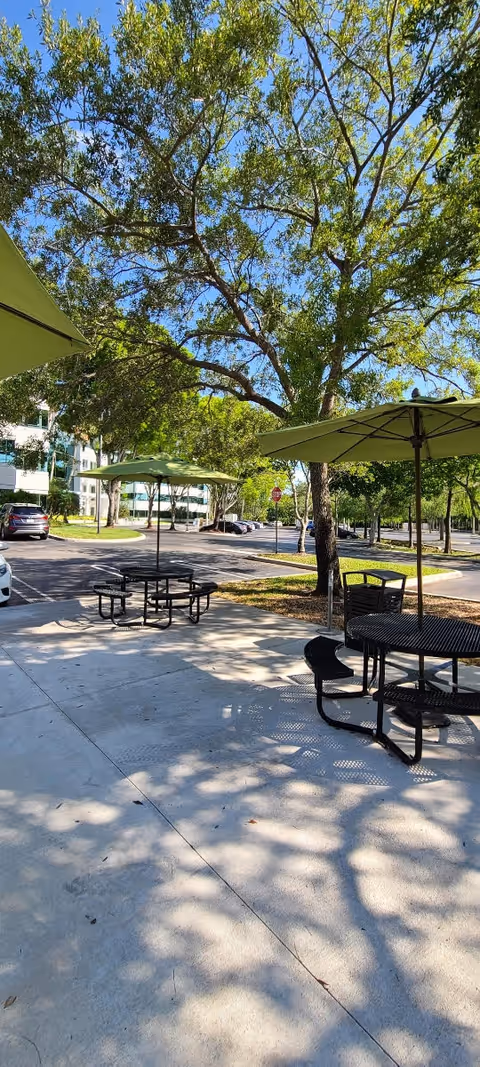 Outdoor courtyard at Elite Care At Home with tables, benches, and shade umbrellas under trees.