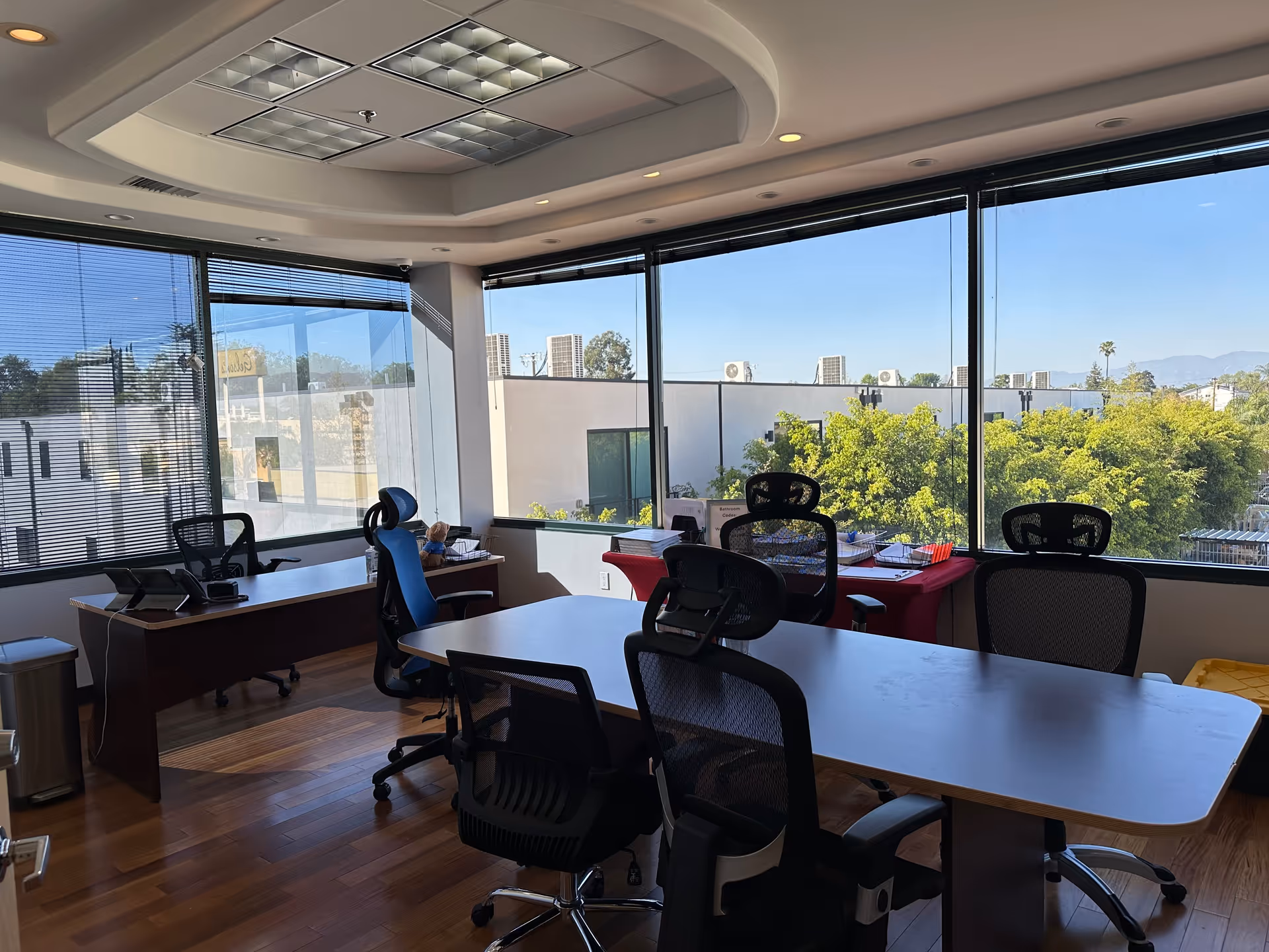 Bright office space with desks, chairs, and expansive windows overlooking trees.