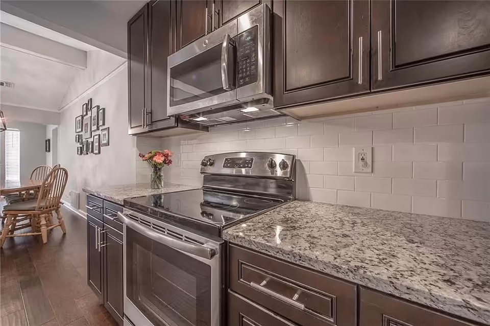 Modern kitchen with dark cabinets, granite countertops, stainless steel appliances, and a dining area.