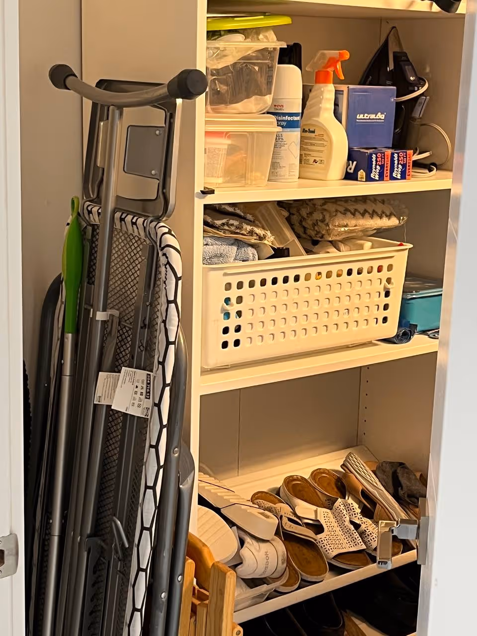 Open closet with shelves featuring cleaning supplies, towels, and multiple pairs of sandals.