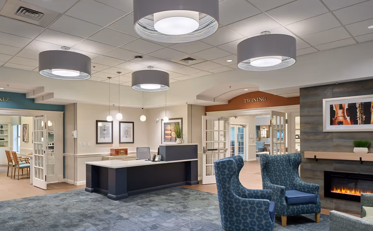 A modern senior living lobby with a reception desk, seating, and a fireplace.