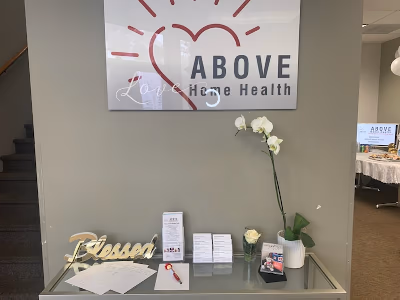 Interior lobby area featuring an ABOVE Home Health sign, staircase, and glass desk.