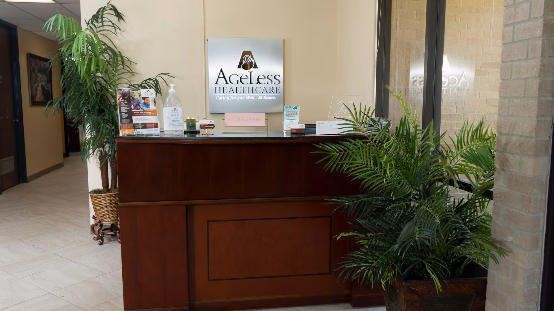 Polished wooden reception desk indoors with Ageless Healthcare sign and lush plants.
